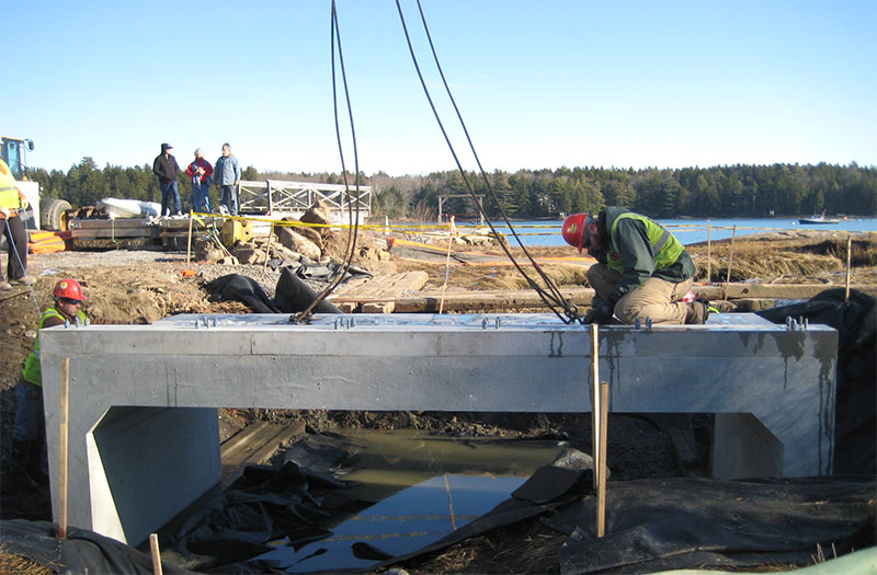 A construction crew installing a concrete structure that allows tidal flow into a creek.