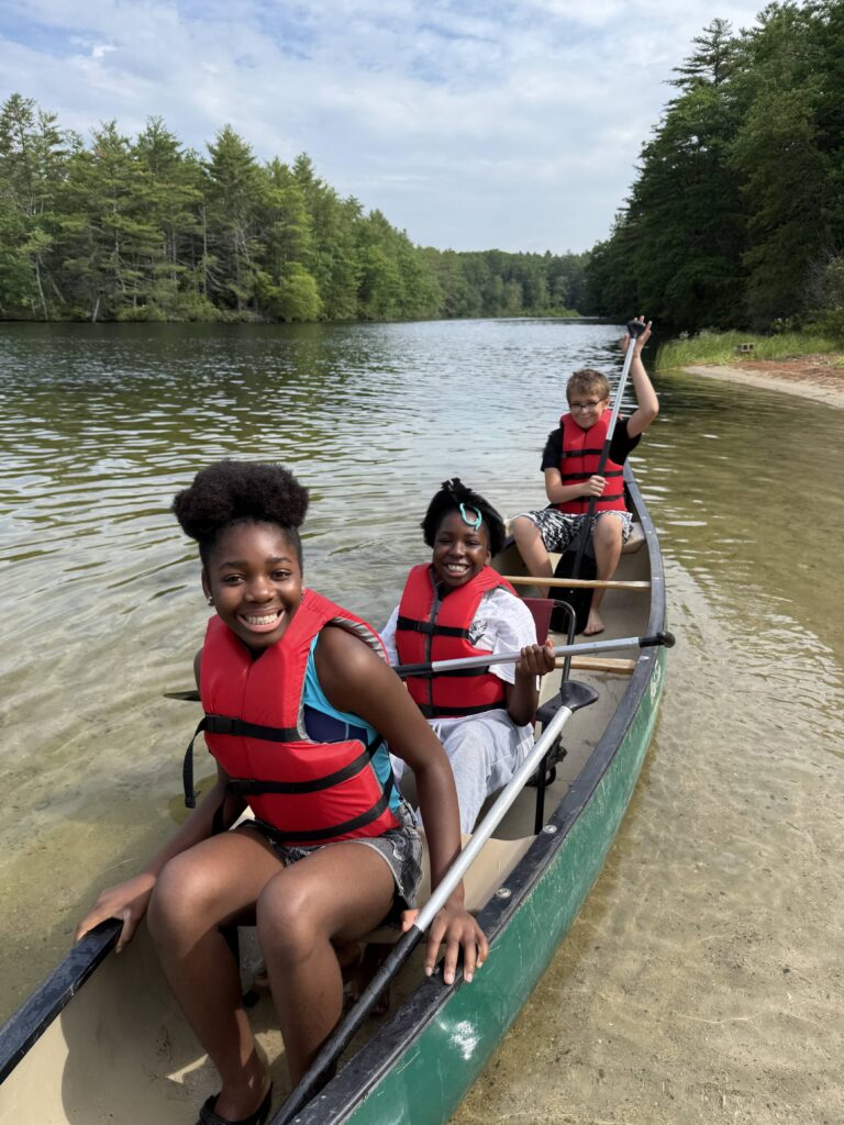 Students are sitting in a canoe on the Presumpscot River, smiling and enjoying the outdoors.